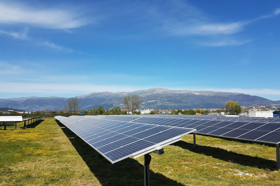 A field of solar panels at a community solar farm. The sky is visible, as well as mountains in the background.