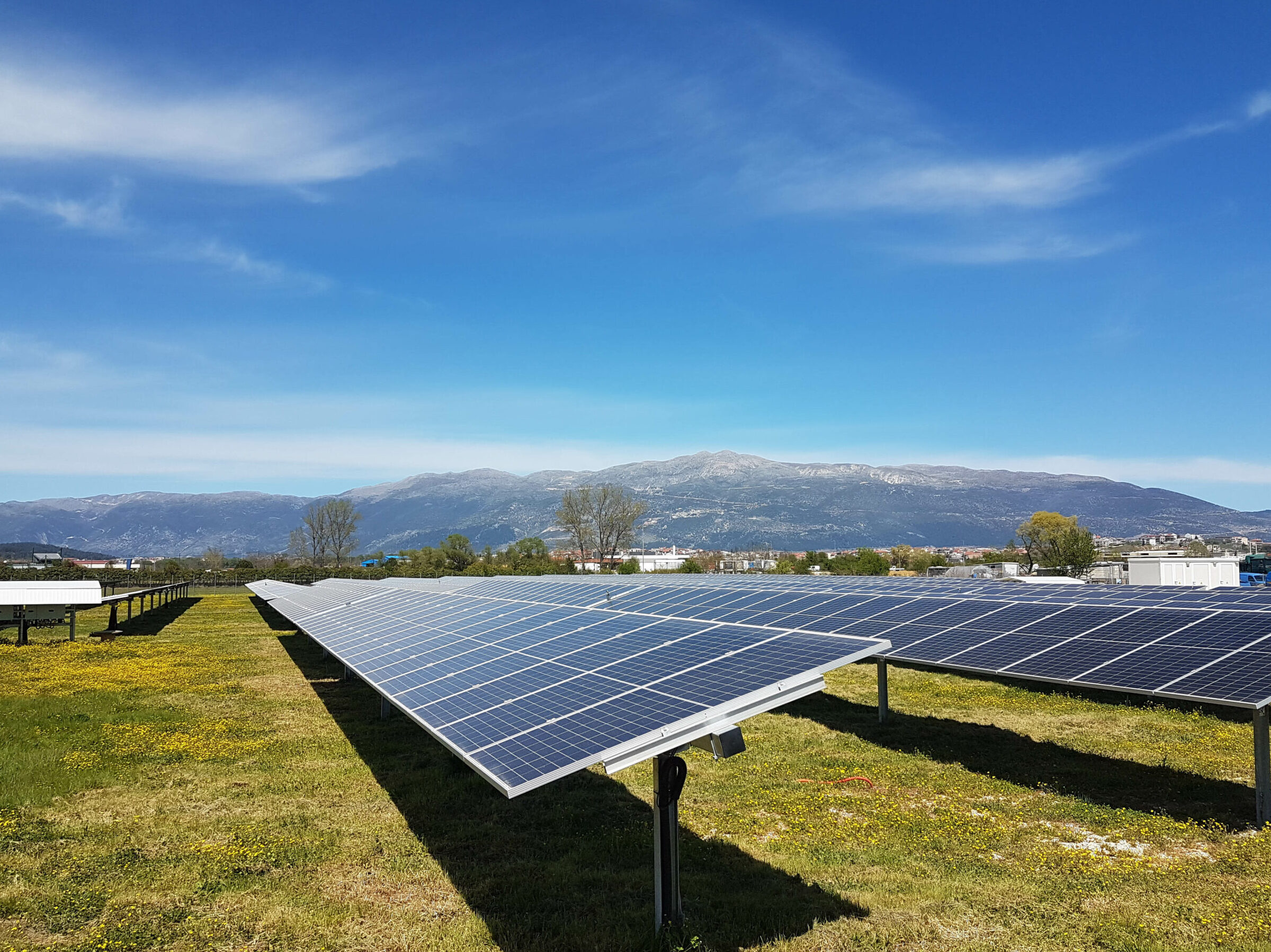 A field of solar panels at a community solar farm. The sky is visible, as well as mountains in the background.