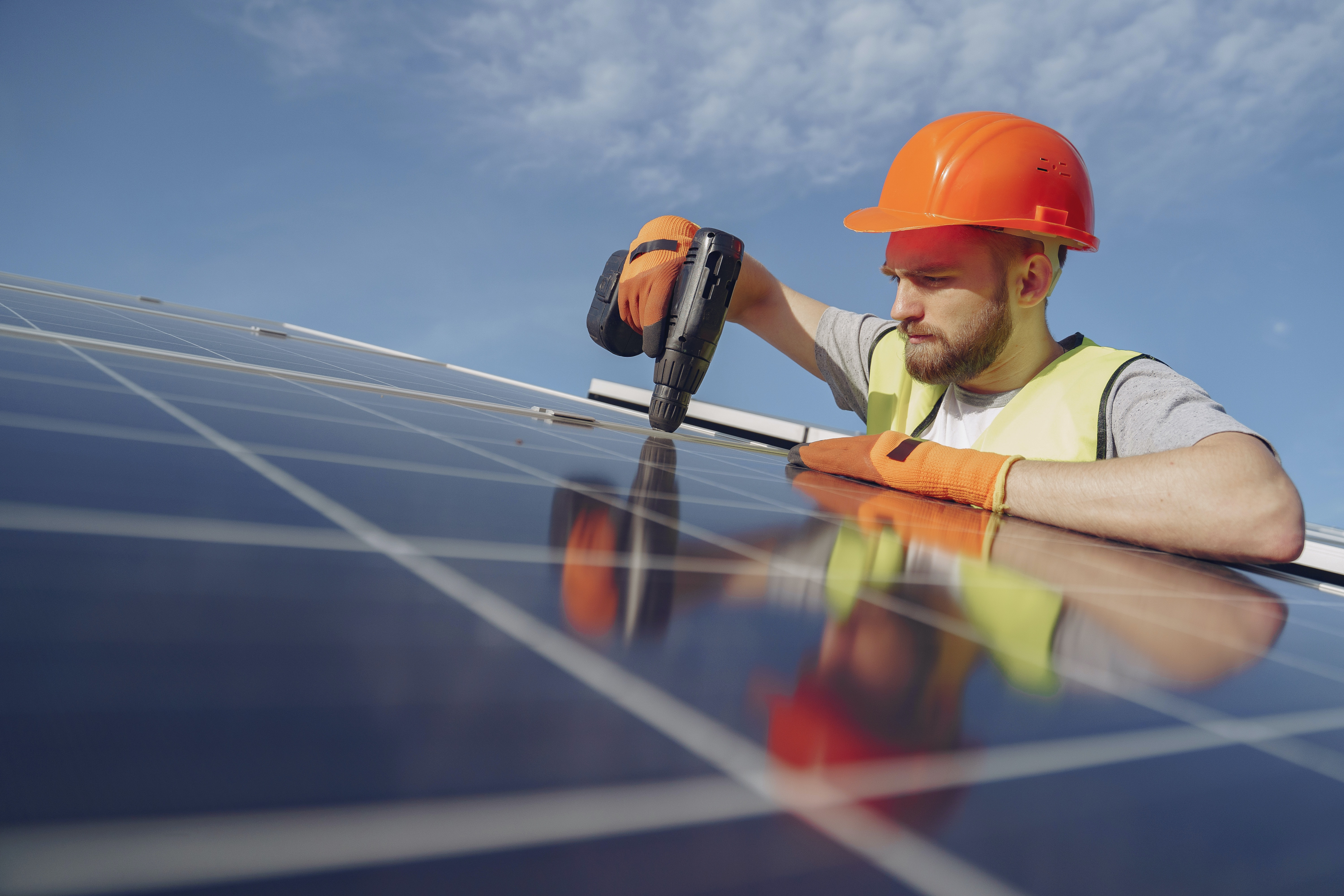 A man holds a drill on a roof while repairing a solar panel installation.